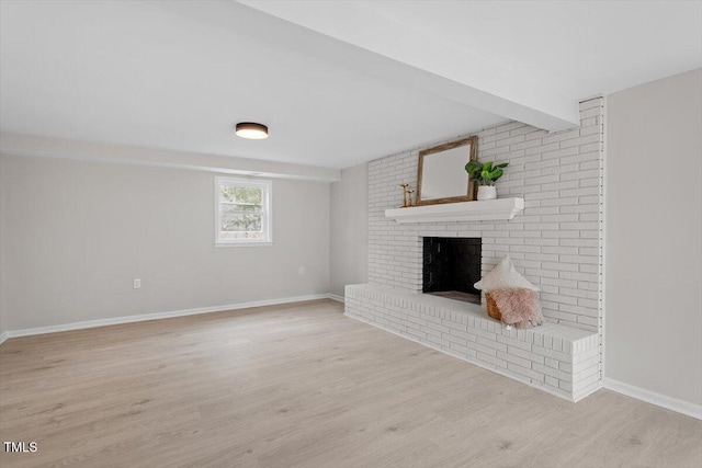 unfurnished living room with beam ceiling, a brick fireplace, and light hardwood / wood-style flooring