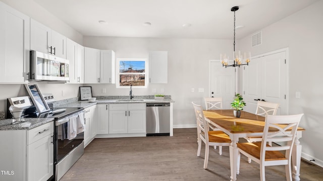 kitchen featuring pendant lighting, sink, light stone countertops, white cabinetry, and stainless steel appliances