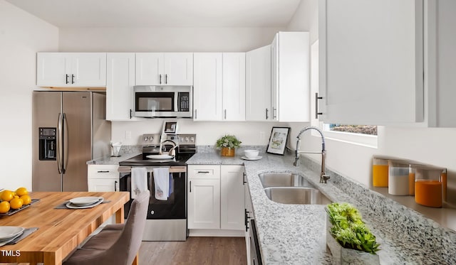 kitchen with light wood-type flooring, light stone counters, stainless steel appliances, sink, and white cabinetry