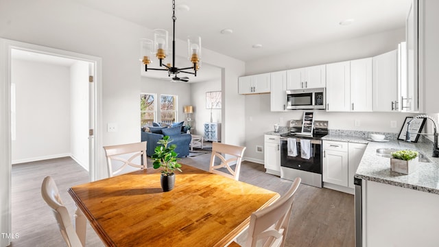 kitchen with white cabinetry, sink, stainless steel appliances, an inviting chandelier, and light stone counters