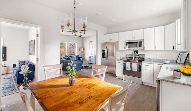 kitchen with white cabinetry, stainless steel appliances, a notable chandelier, pendant lighting, and wood-type flooring