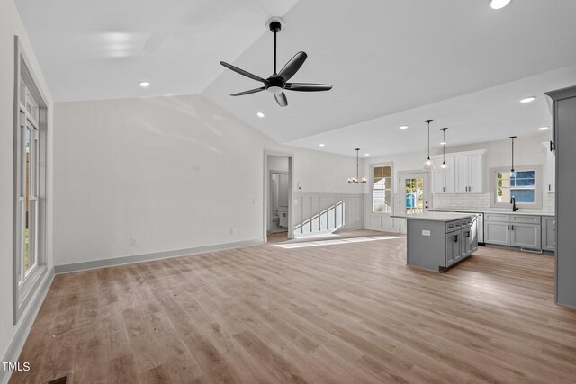 unfurnished living room with ceiling fan with notable chandelier, light hardwood / wood-style floors, sink, and vaulted ceiling