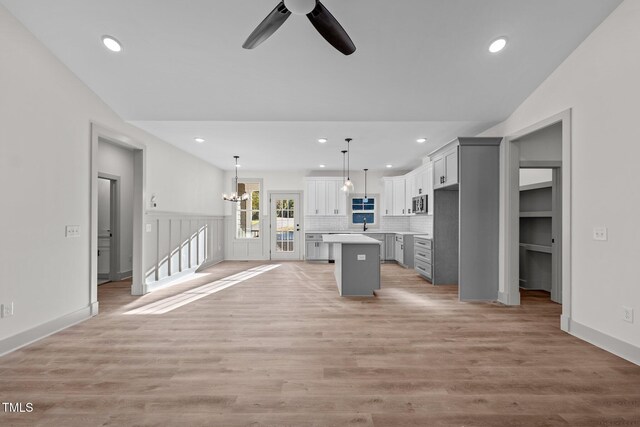 unfurnished living room with ceiling fan with notable chandelier, light hardwood / wood-style flooring, vaulted ceiling, and sink