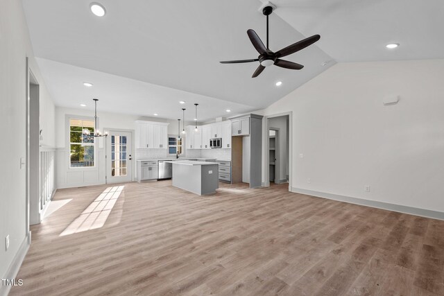 unfurnished living room featuring ceiling fan with notable chandelier, high vaulted ceiling, and light hardwood / wood-style flooring