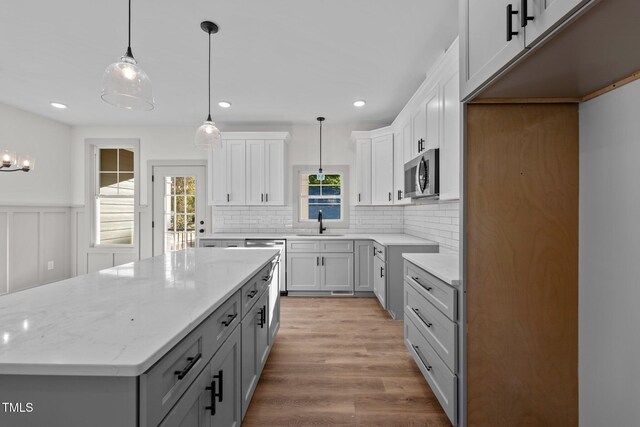 kitchen featuring white cabinetry, a center island, light stone countertops, and decorative light fixtures