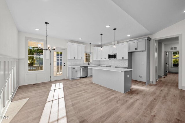 kitchen featuring backsplash, stainless steel appliances, a kitchen island, hanging light fixtures, and lofted ceiling