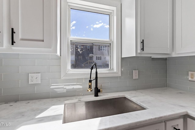 kitchen featuring white cabinets, backsplash, light stone countertops, and sink