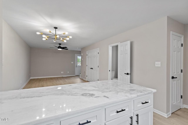 kitchen with white cabinets, ceiling fan with notable chandelier, light hardwood / wood-style floors, and light stone counters