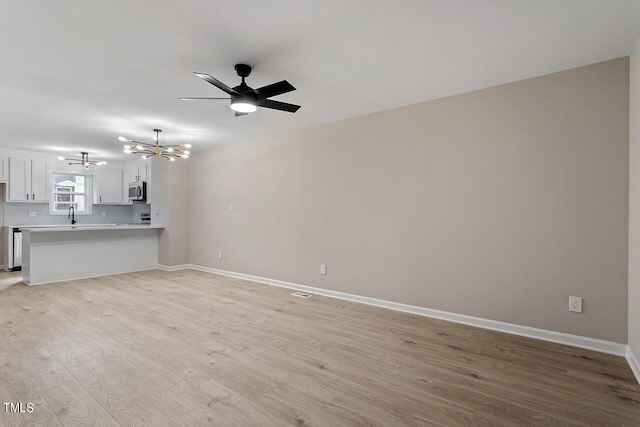 unfurnished living room featuring ceiling fan with notable chandelier, light wood-type flooring, and sink