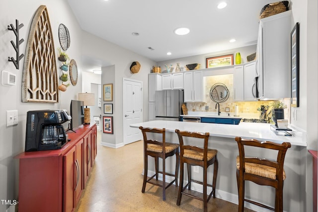 kitchen with white cabinetry, sink, stainless steel appliances, backsplash, and kitchen peninsula