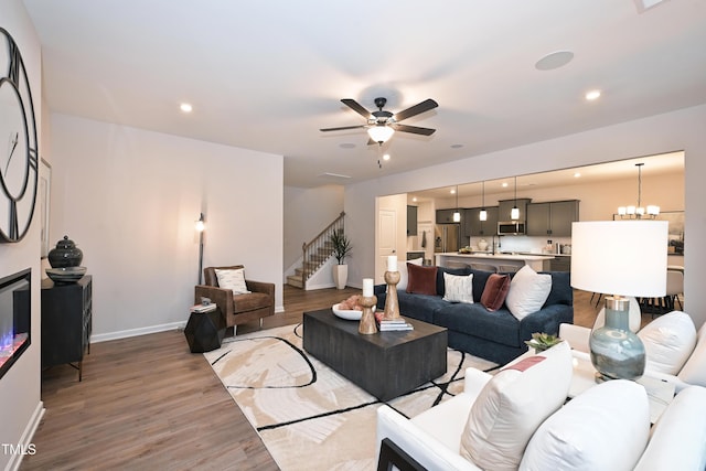 living room featuring ceiling fan with notable chandelier and light hardwood / wood-style flooring