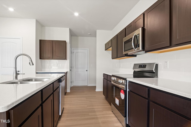 kitchen with sink, appliances with stainless steel finishes, dark brown cabinets, tasteful backsplash, and light wood-type flooring