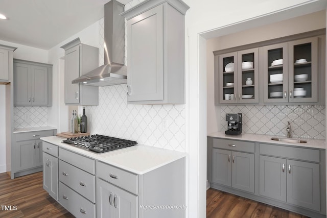 kitchen featuring wall chimney range hood, stainless steel gas cooktop, gray cabinetry, and sink