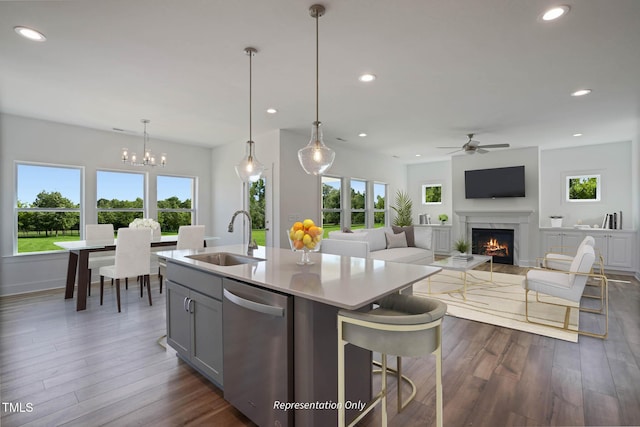 kitchen with stainless steel dishwasher, ceiling fan with notable chandelier, sink, hanging light fixtures, and an island with sink