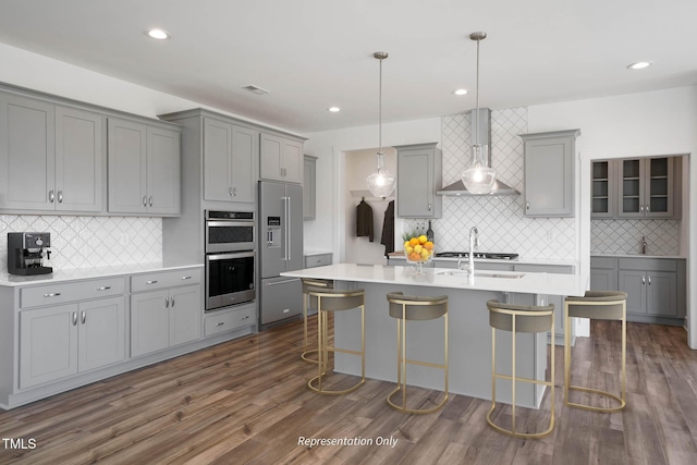 kitchen featuring gray cabinetry, wall chimney exhaust hood, hanging light fixtures, stainless steel appliances, and a breakfast bar area