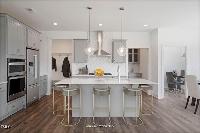 kitchen featuring appliances with stainless steel finishes, gray cabinetry, sink, wall chimney range hood, and pendant lighting