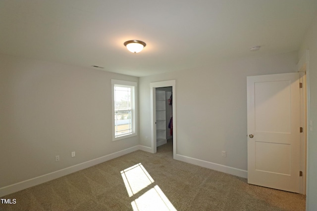 unfurnished bedroom with a walk in closet, a closet, and light colored carpet