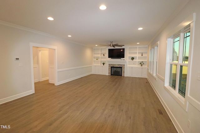 unfurnished living room with crown molding, hardwood / wood-style flooring, ceiling fan, built in features, and a fireplace