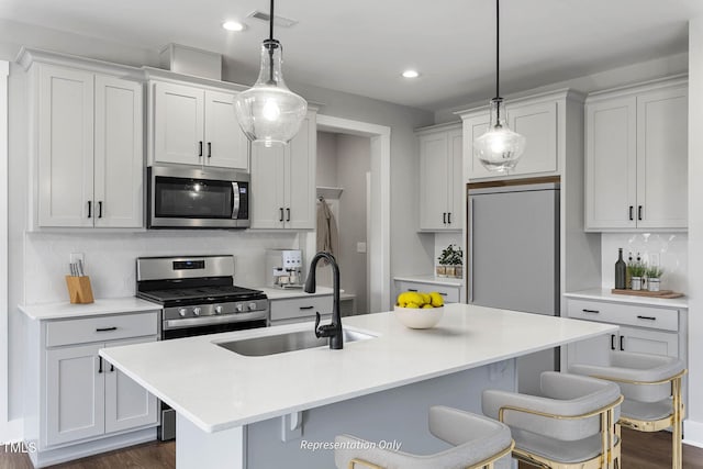 kitchen with tasteful backsplash, stainless steel appliances, sink, hanging light fixtures, and an island with sink