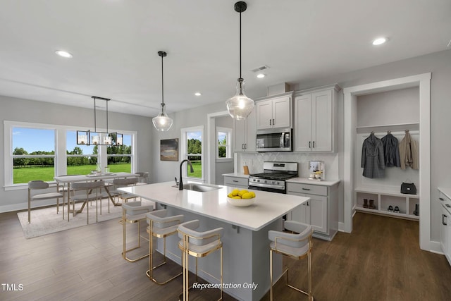 kitchen with decorative light fixtures, sink, stainless steel appliances, and a kitchen island with sink