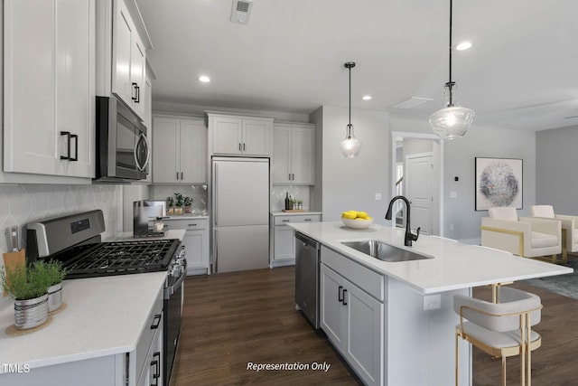 kitchen with tasteful backsplash, stainless steel appliances, sink, hanging light fixtures, and an island with sink