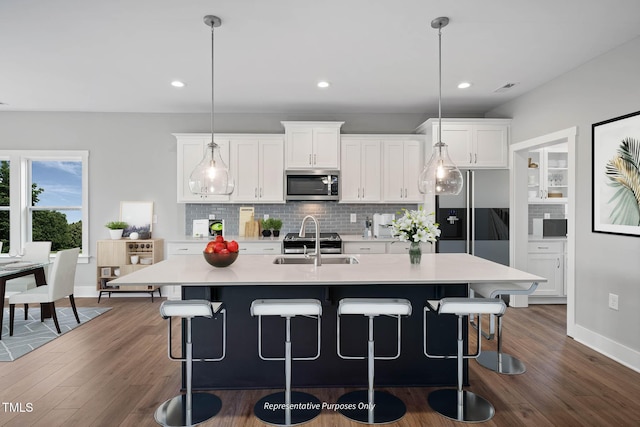 kitchen featuring appliances with stainless steel finishes, sink, white cabinetry, hanging light fixtures, and an island with sink