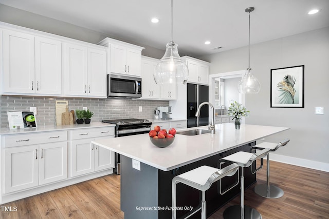 kitchen with sink, stainless steel appliances, decorative light fixtures, a kitchen island with sink, and white cabinets