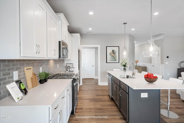 kitchen with a center island with sink, white cabinets, stainless steel appliances, and decorative light fixtures