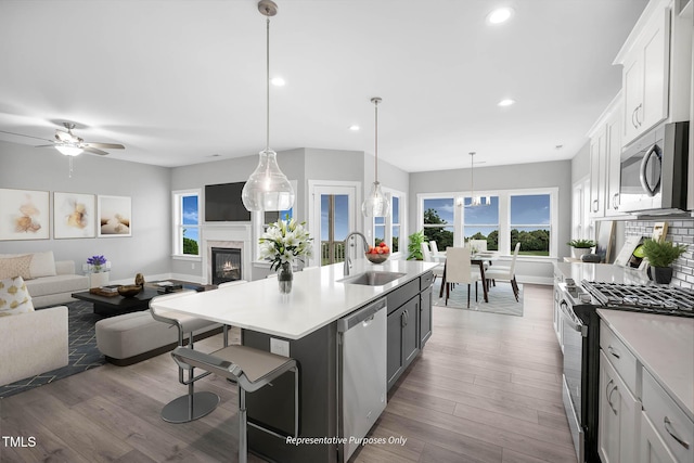 kitchen featuring hanging light fixtures, sink, an island with sink, appliances with stainless steel finishes, and white cabinetry