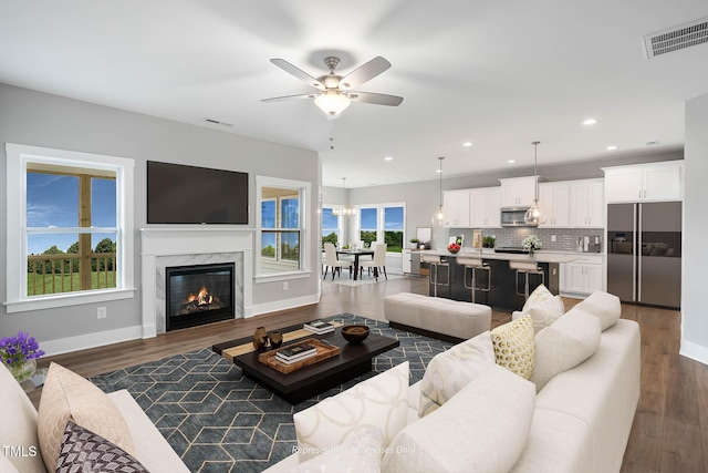 living room featuring a wealth of natural light, ceiling fan, dark wood-type flooring, and a premium fireplace