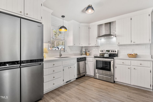 kitchen with sink, stainless steel appliances, wall chimney range hood, pendant lighting, and white cabinets