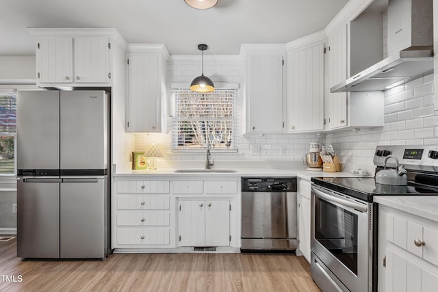 kitchen with stainless steel appliances, sink, wall chimney range hood, white cabinets, and hanging light fixtures