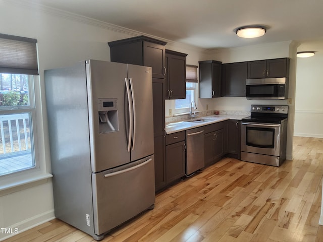 kitchen featuring stainless steel appliances, ornamental molding, sink, and light hardwood / wood-style floors