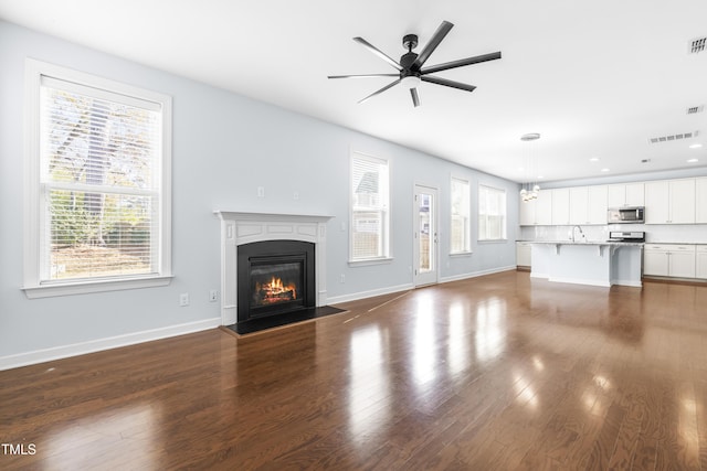 unfurnished living room featuring ceiling fan with notable chandelier, a wealth of natural light, dark wood-type flooring, and sink