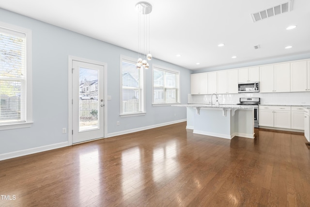 kitchen with a kitchen breakfast bar, an island with sink, appliances with stainless steel finishes, tasteful backsplash, and decorative light fixtures