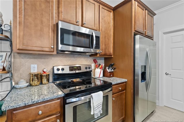 kitchen with light stone counters, backsplash, crown molding, light tile patterned floors, and appliances with stainless steel finishes