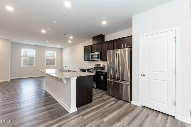 kitchen with hardwood / wood-style floors, a center island with sink, a kitchen breakfast bar, sink, and stainless steel appliances