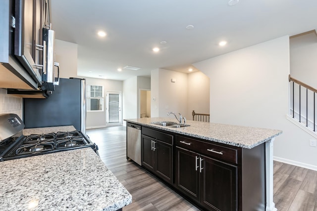 kitchen with light stone countertops, stainless steel appliances, a kitchen island with sink, and sink