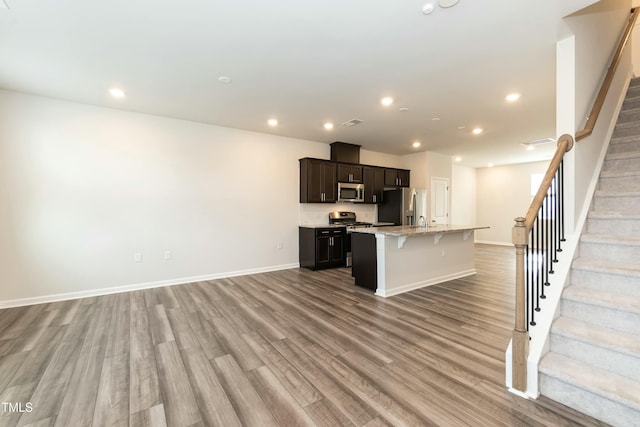 kitchen with a breakfast bar, a kitchen island with sink, light hardwood / wood-style flooring, appliances with stainless steel finishes, and light stone counters