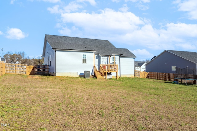 rear view of house featuring central AC, a wooden deck, a trampoline, and a lawn