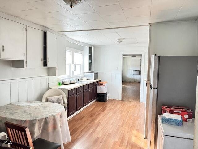 kitchen with stainless steel fridge, light wood-type flooring, dark brown cabinetry, sink, and white cabinetry