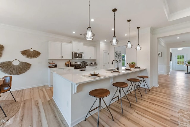 kitchen with appliances with stainless steel finishes, ornamental molding, white cabinetry, a sink, and a kitchen bar