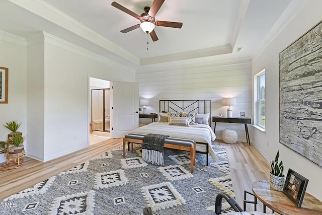 bedroom with ensuite bath, ceiling fan, crown molding, a tray ceiling, and light wood-type flooring