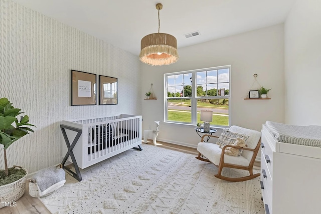 bedroom with an accent wall, wood finished floors, visible vents, baseboards, and wallpapered walls