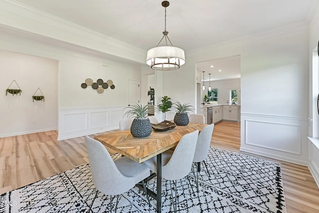 dining space featuring light wood-type flooring, wainscoting, crown molding, and a decorative wall