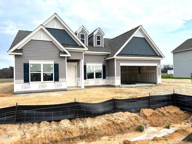 view of front facade featuring board and batten siding, roof with shingles, a garage, and fence