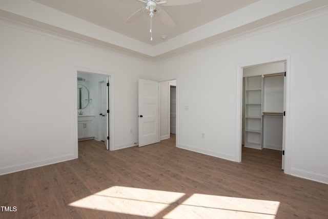 unfurnished bedroom featuring a spacious closet, baseboards, ensuite bathroom, wood finished floors, and a closet