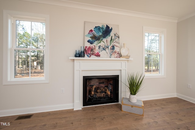 unfurnished living room featuring wood finished floors, visible vents, baseboards, a fireplace, and crown molding