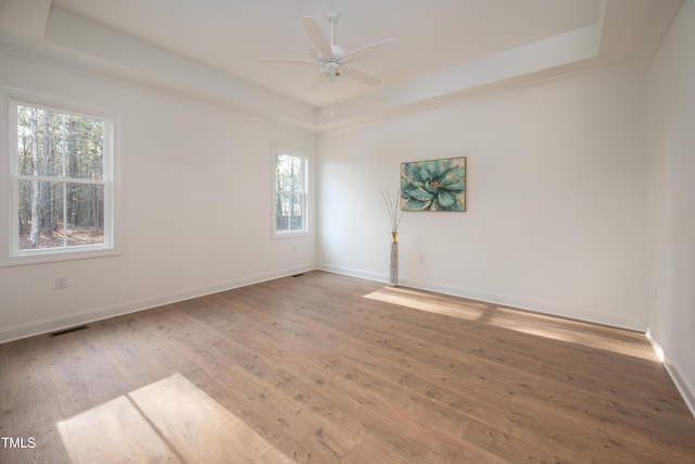 empty room featuring ceiling fan, baseboards, a raised ceiling, and wood-type flooring