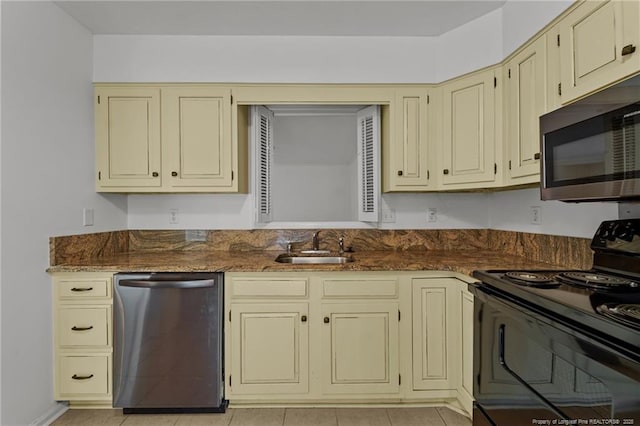 kitchen featuring dark stone counters, sink, light tile patterned floors, appliances with stainless steel finishes, and cream cabinetry